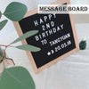 A wooden message board with chalk writing that says Happy 2nd Birthday to Tangyuan on a white cloth.