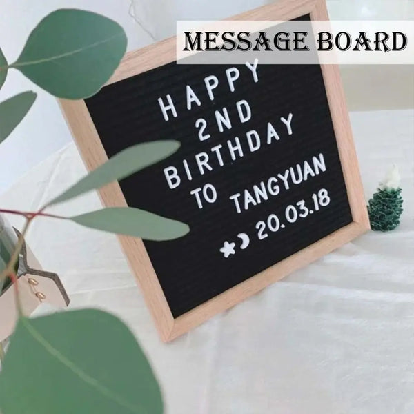 A wooden message board with chalk writing that says Happy 2nd Birthday to Tangyuan on a white cloth.