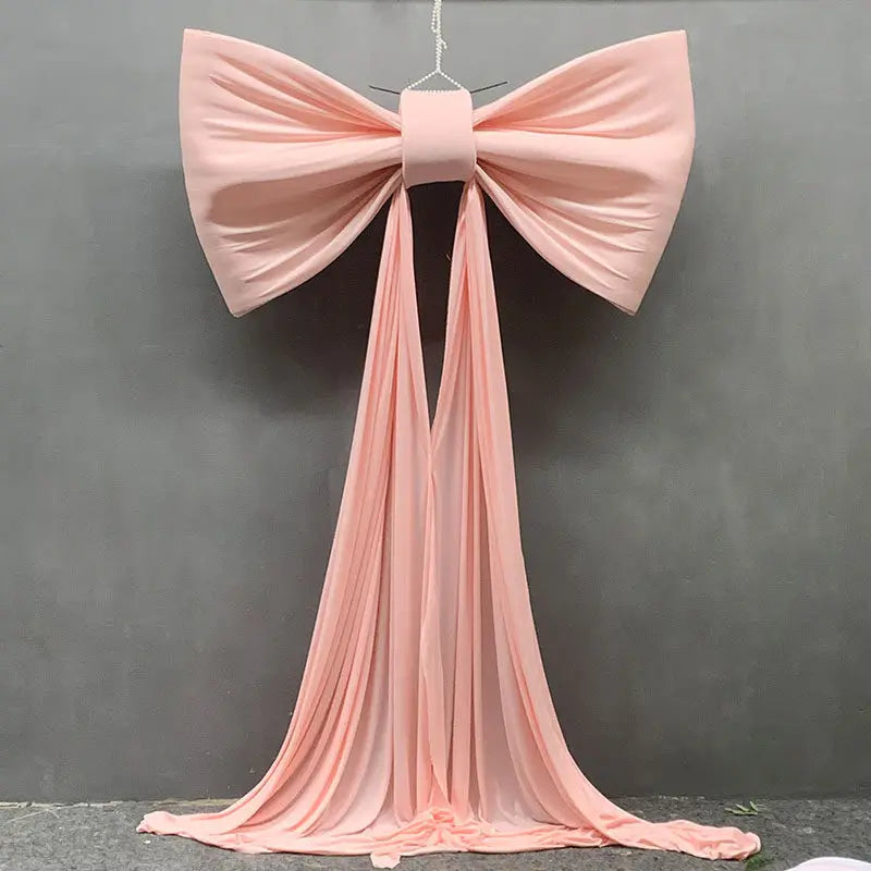 A pink satin bow with long tulle drape hanging against a gray wall.