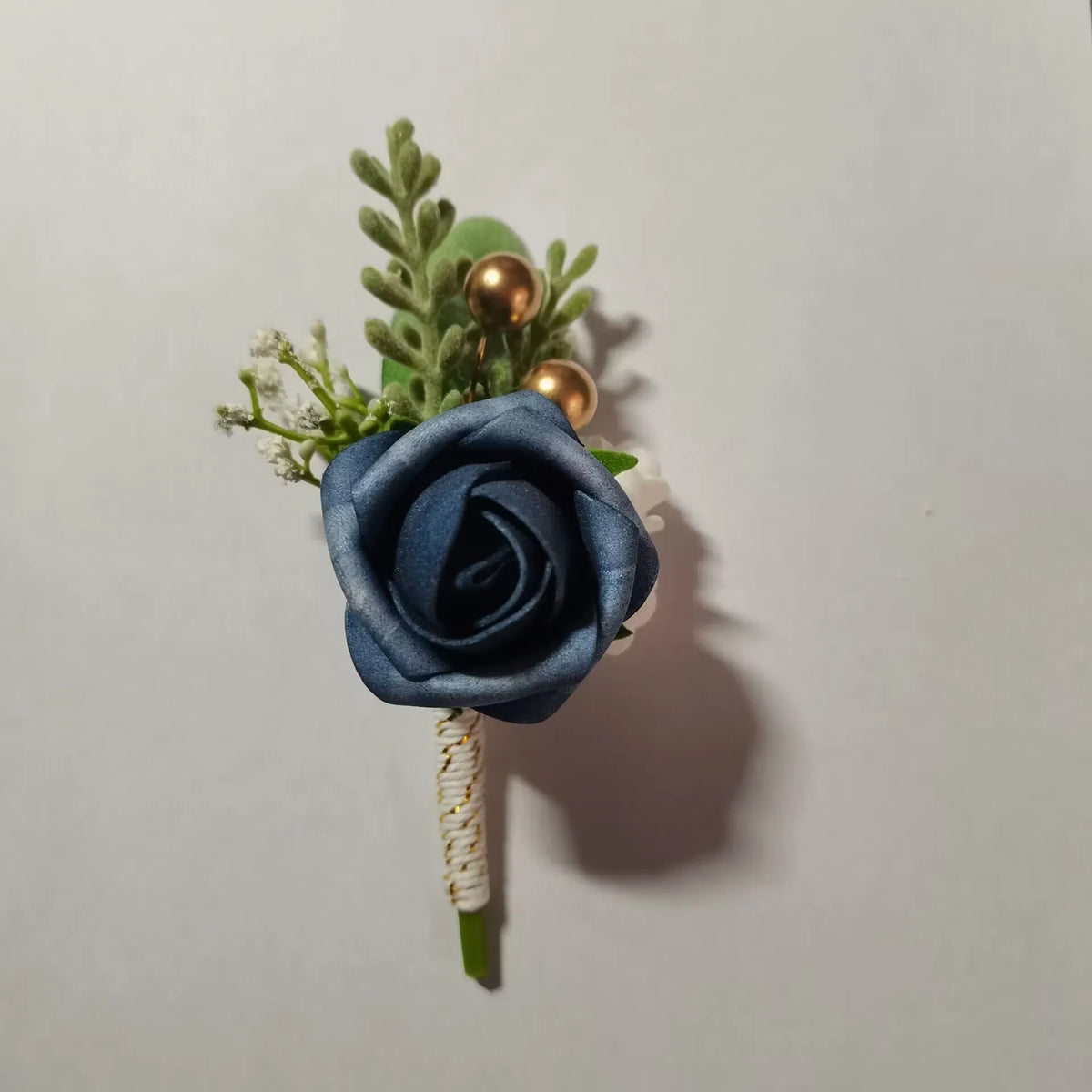A small bouquet featuring a dusty blue silk rose, green foliage, and gold accents.