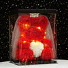 A red artificial rose teddy bear with white accents displayed in a clear box against a dark background.