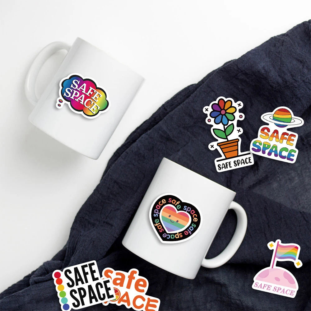 A white mug with colorful safe space graffiti stickers on the side, placed on a dark fabric.