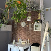 A white table is set against a textured brick wall decorated with various plants and hanging decor.