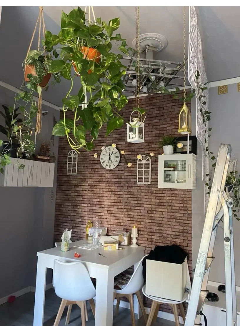 A white table is set against a textured brick wall decorated with various plants and hanging decor.