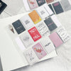 A collection of square, colorful stickers and labels arranged on a white grid binder sheet.