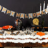 A Halloween decor display featuring a black pumpkin, a golden skull, and a banner strung with black and orange pennants.