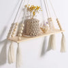 Handmade macrame wood wall shelf featuring a natural fiber plant arrangement and decorative tassels.