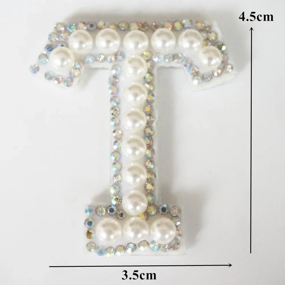 A rhinestone patch shaped like the letter T, featuring white pearls and blue crystals.