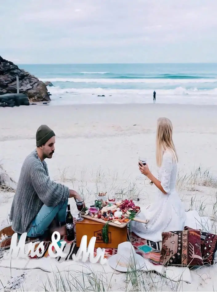 A couple sits on a beach with wooden letters spelling Mr and Mrs in the sand.