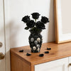 A black gothic skull resin decorative vase filled with dark roses sits on a wooden surface.
