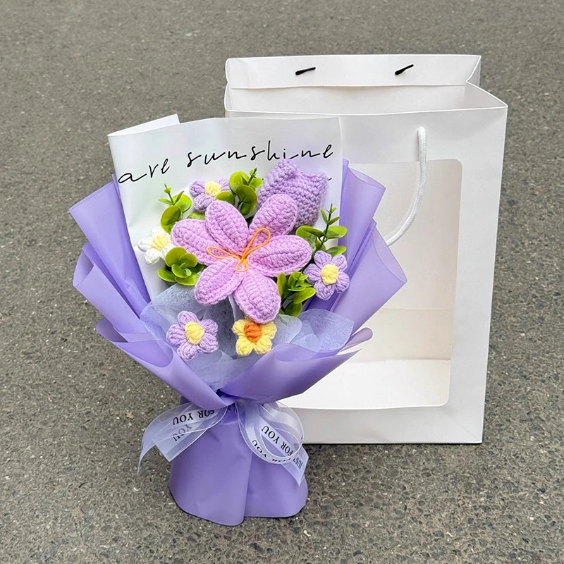 A bouquet of handmade purple and yellow crochet flowers tied with a ribbon, presented in a white paper bag.