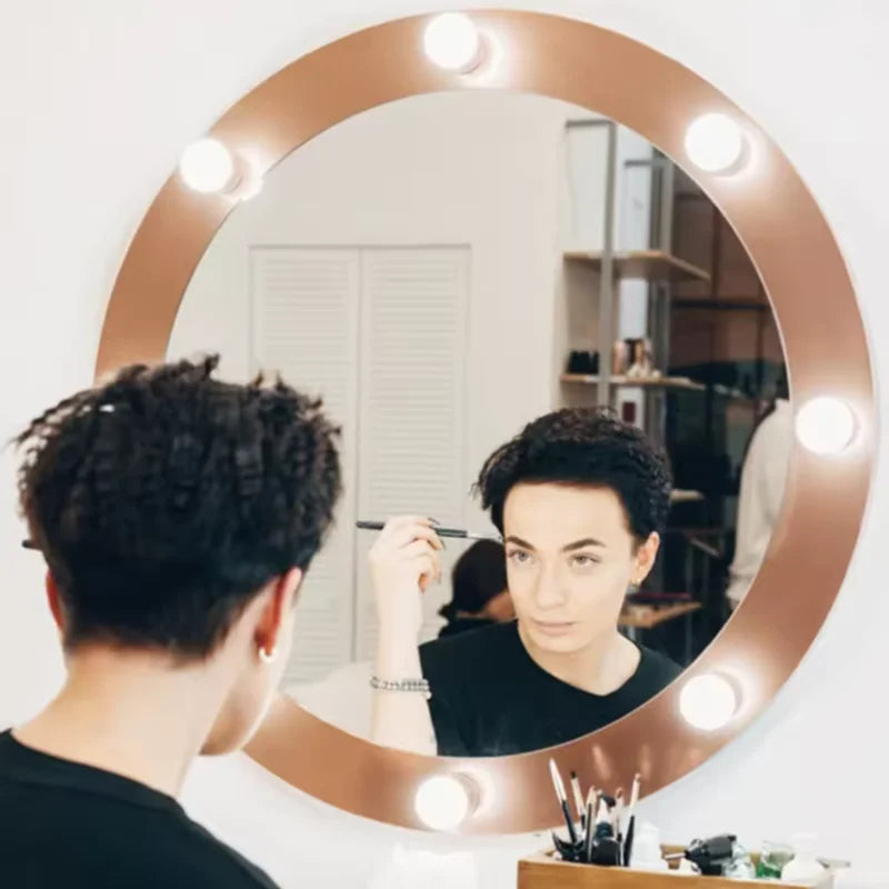 A person is looking into a round, rose gold-framed dimmable LED vanity mirror while applying makeup.
