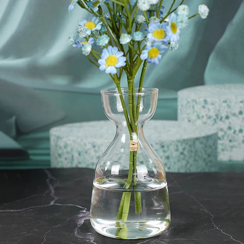 A glass vase holds a bouquet of blue and yellow flowers, set against a muted teal background.