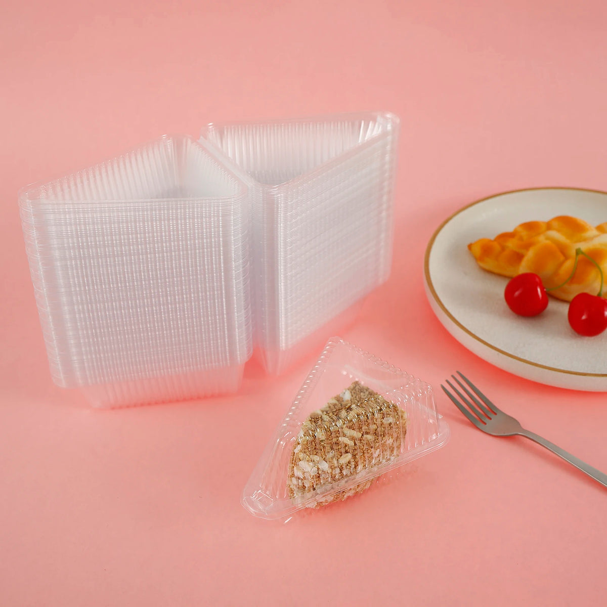 Clear reusable triangle containers holding cake slices on a pink background.