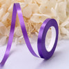 Purple satin balloon ribbon roll unwinding against a background of white flowers.