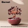 A handcrafted garnet crystal tree with a copper wire base sits in a pink stone bowl.