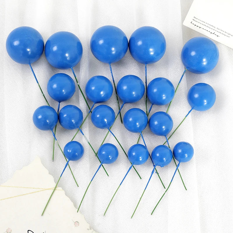 A set of twenty bright blue spherical ball cake toppers with thin green stems arranged on a white background.