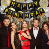 A group of five people posing in front of a banner that reads Happy Birthday made of black and gold decorations.