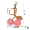 A gold-toned resin pink cherry pendant keychain with a leaf charm and a chain.