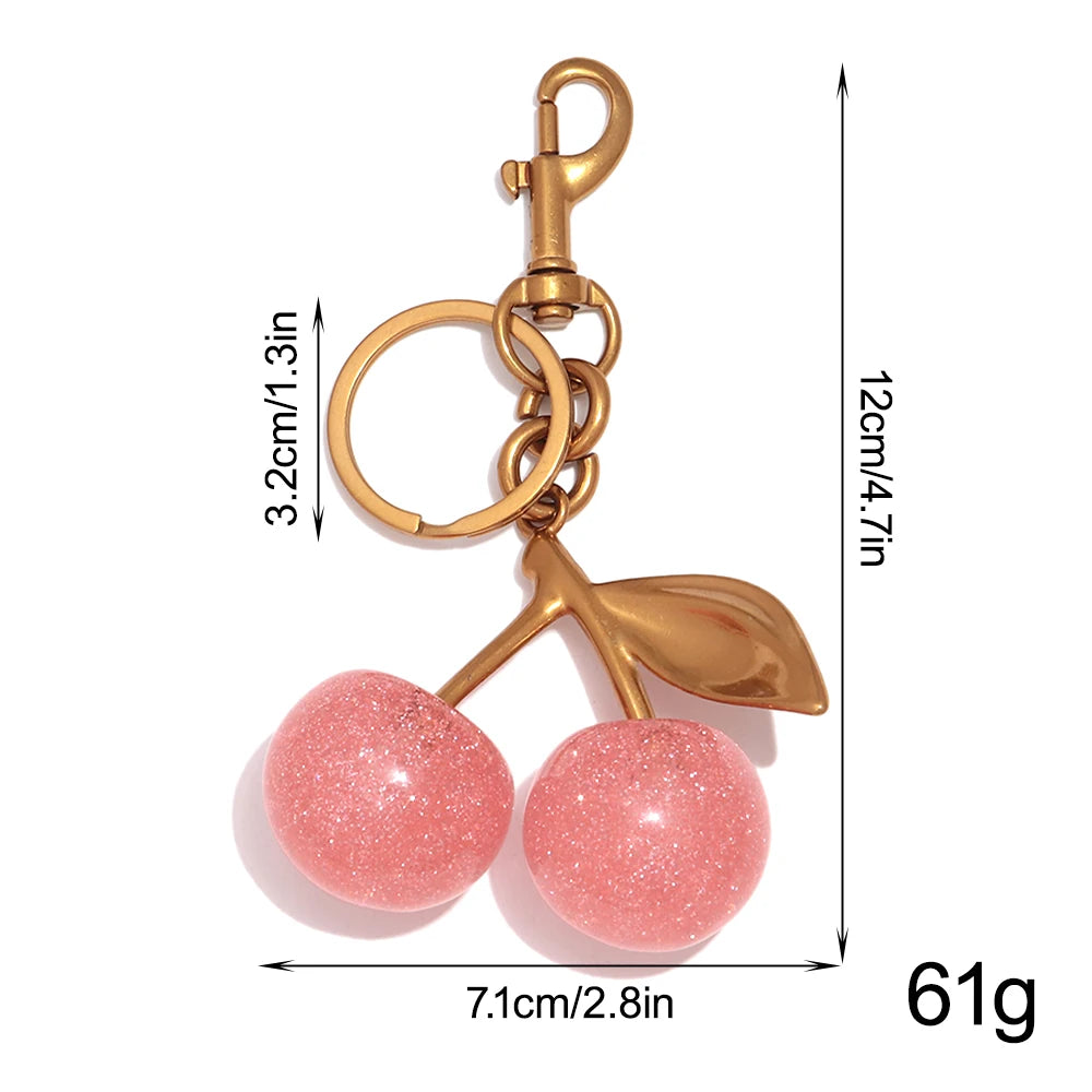 A gold-toned resin pink cherry pendant keychain with a leaf charm and a chain.