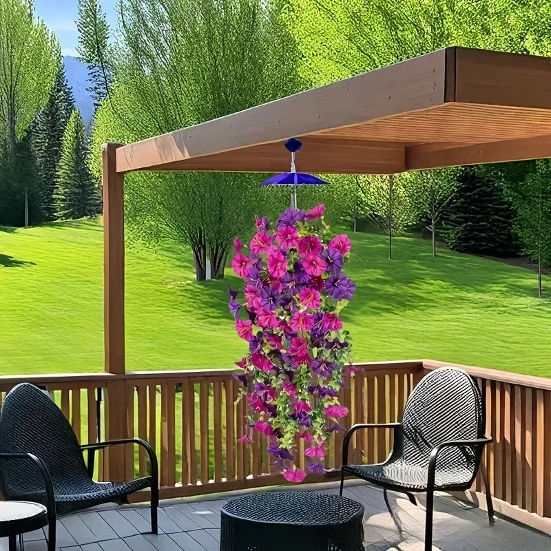 A purple morning glory garland hangs in front of a wooden deck railing with green trees in the background.