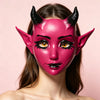 A woman wearing a vibrant pink horned fantasy creature mask with detailed eye makeup.