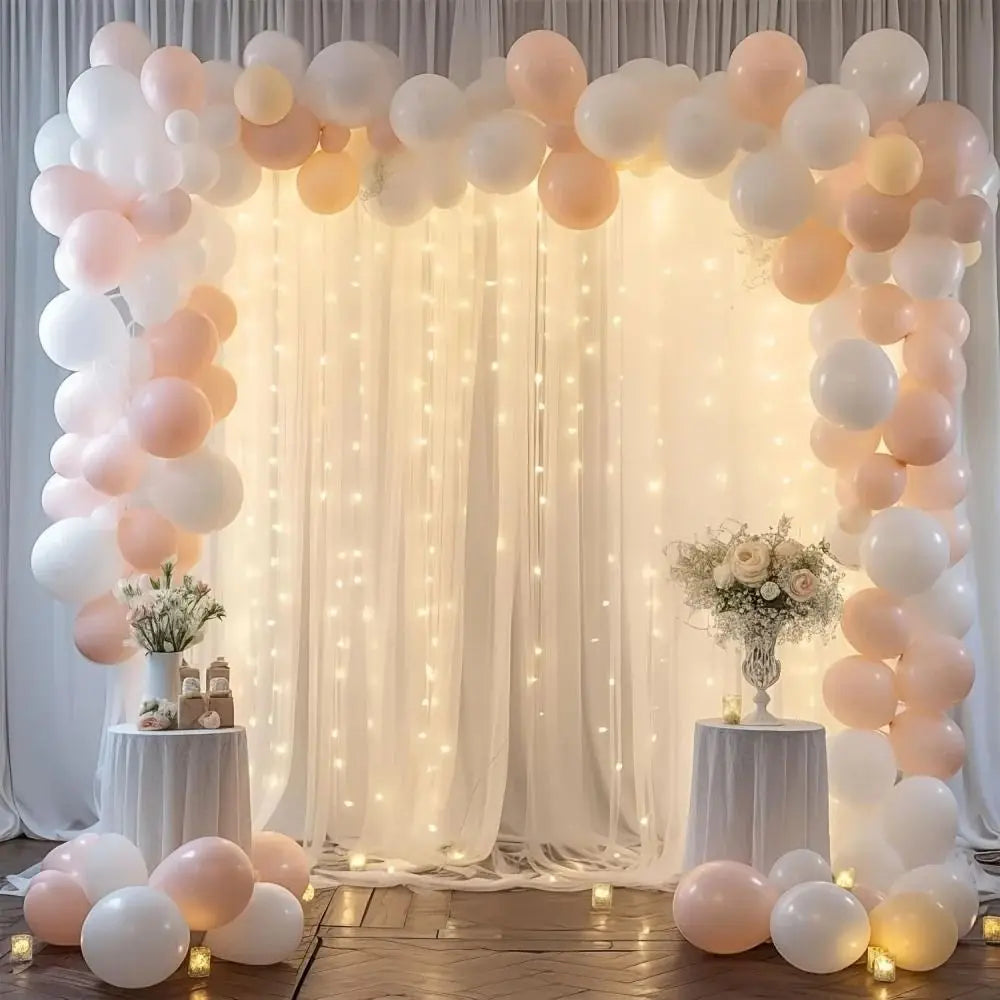 Elegant white wedding tulle backdrop decorated with light pink and white balloons and string lights