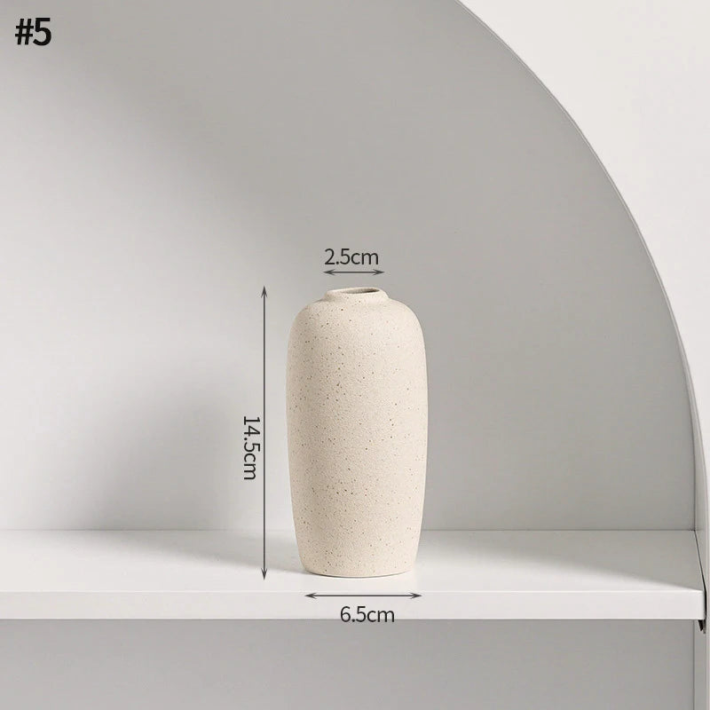 A beige minimalist ceramic vase with a round body is displayed on a white shelf.