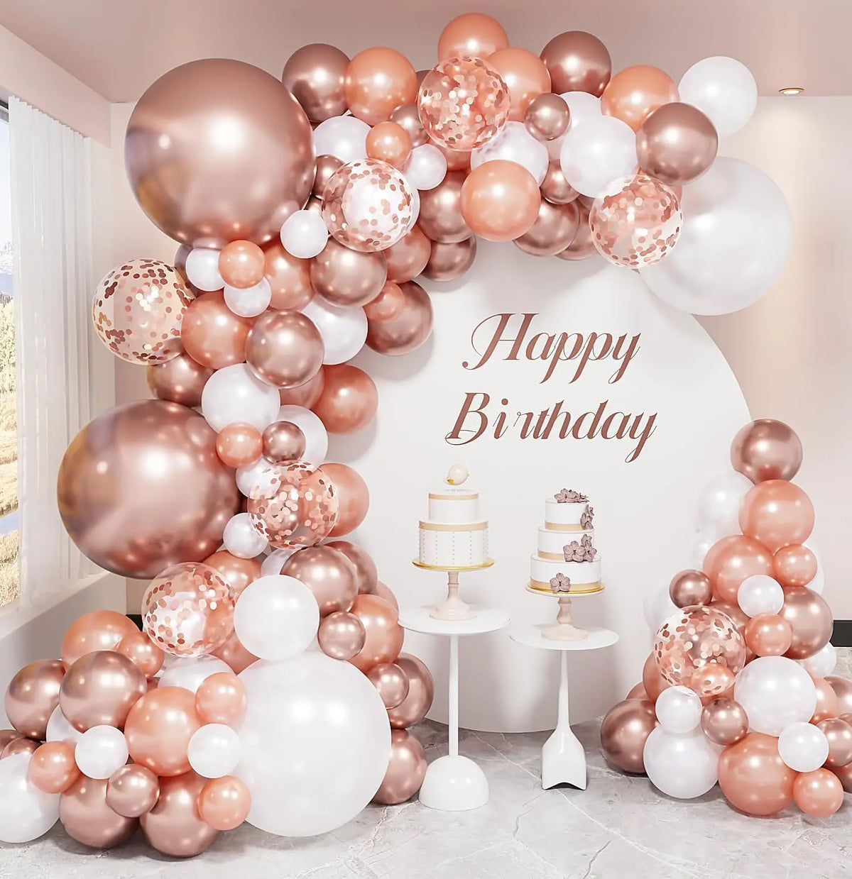 A large balloon garland featuring rose gold, pink, and white balloons arranged in an arch for a birthday celebration.