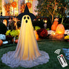 A large, glowing white ghost decoration with black features stands in a garden setting.