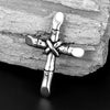 A silver stainless steel cross necklace pendant resting on a piece of weathered wood.