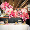 A display of pastel pink and white latex balloons with metallic confetti accents arranged on a table.