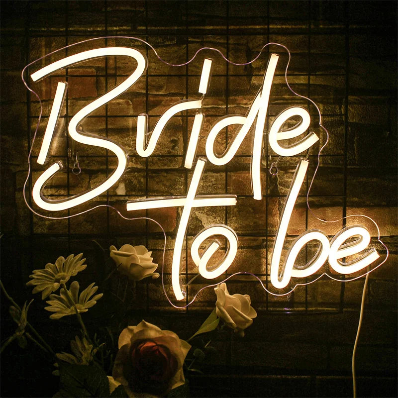 A neon sign spelling 'Bride to be' illuminates white roses against a dark, textured background.