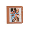 A brown PU leather photo album with a clear window displaying instant camera prints and mementos.