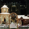 A display featuring a white plush Christmas tree skirt with snowflake designs surrounded by decorated miniature buildings and