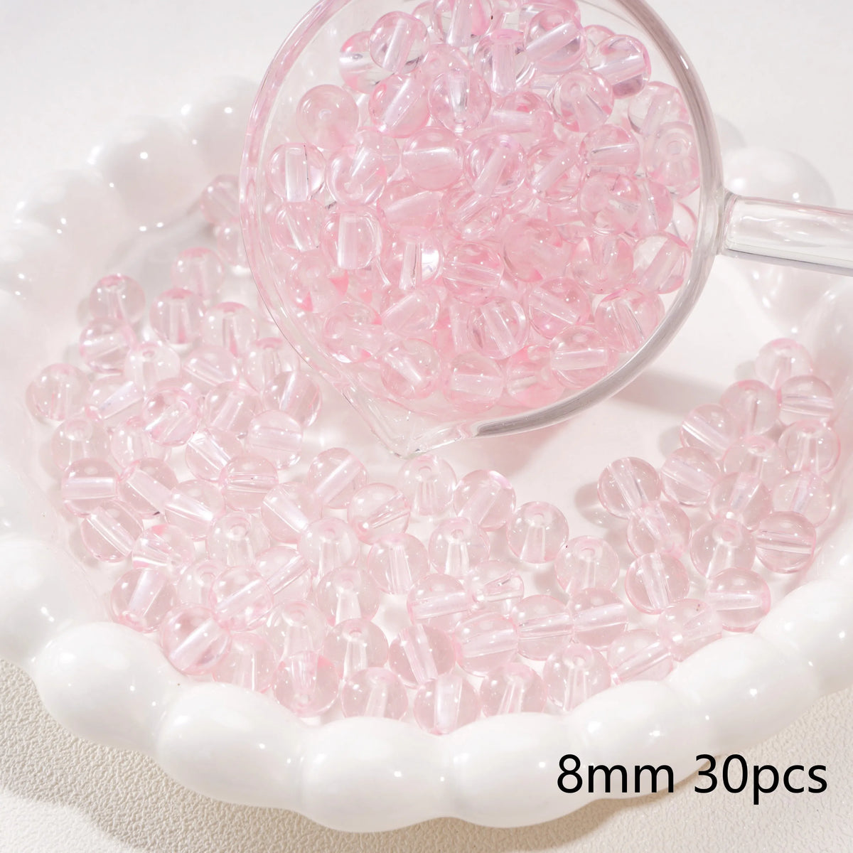 A clear glass bowl filled with pink round spacer beads for jewelry making, displayed on a white dish.
