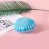 A translucent blue seashell resting on a pink surface next to a green palm frond.