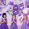 Three young girls in purple dresses pose with large purple musical number balloons