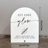A white acrylic sign with black script text that reads Let Love glow and features an illustration of a glow stick.