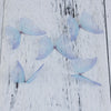 Light blue organza butterfly embellishments scattered on a white wooden surface.