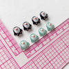 A collection of resin mini penguin figurines in black and light green colors arranged on a pink ruler.