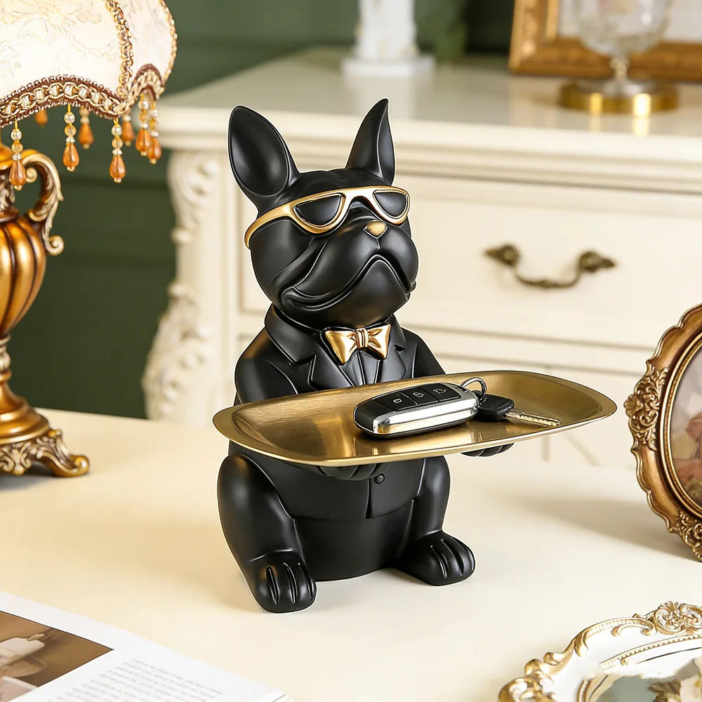 A black bulldog figurine wearing sunglasses and holding a gold tray on a light surface.