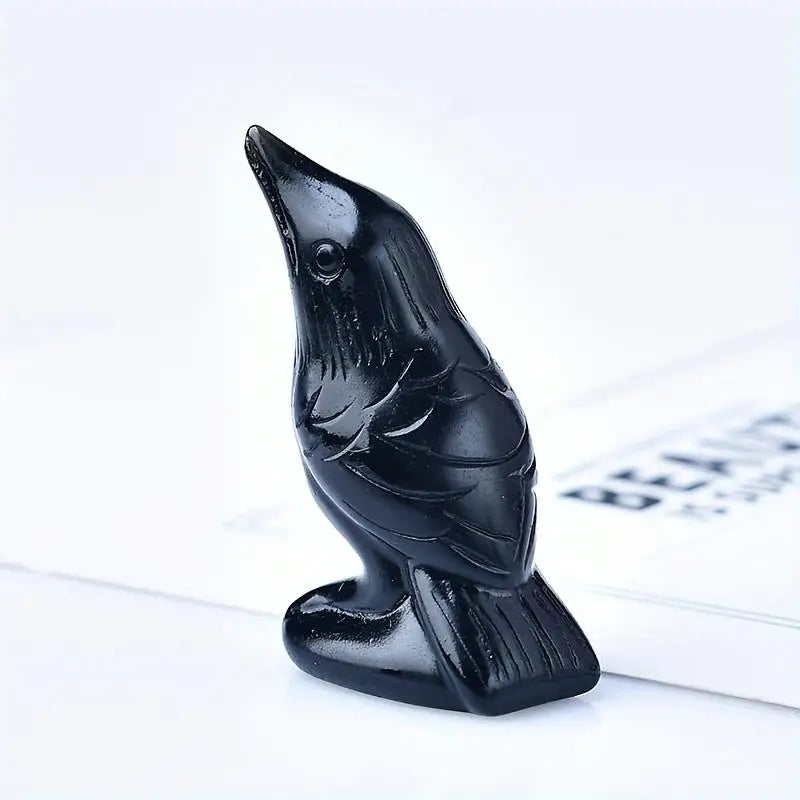 A black handcrafted obsidian crow statue sitting on a white surface.