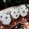 White latex football party balloons are tied to a wooden surface with sunlight filtering through the leaves.