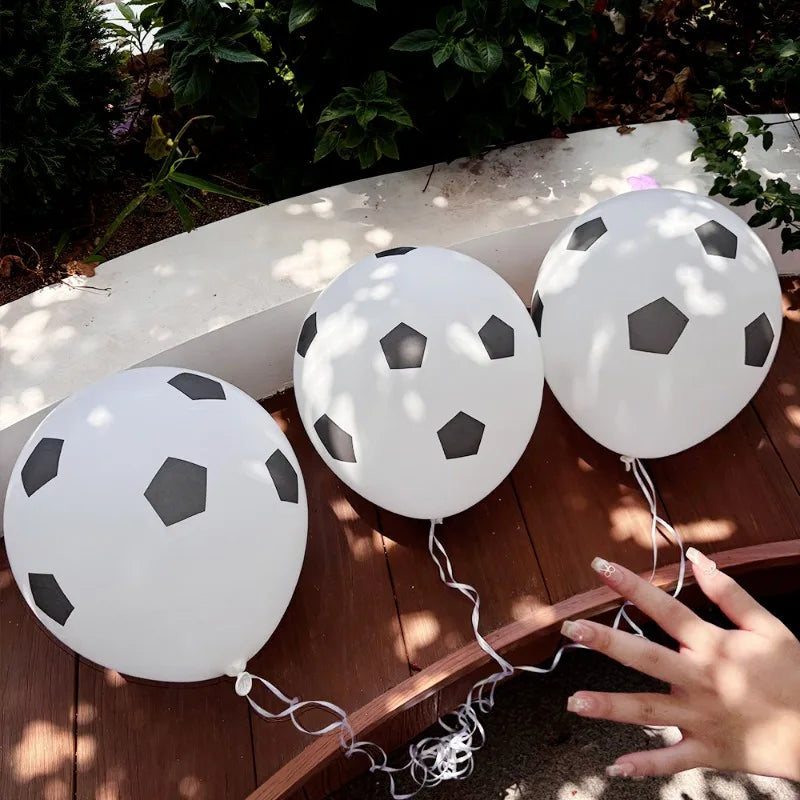 White latex football party balloons are tied to a wooden surface with sunlight filtering through the leaves.