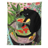A black cat sits on a table with goldfish in a glass bowl, set against a floral tapestry background.