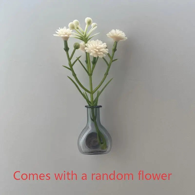 A small glass vase holds a sprig of white flowers on a light gray background.