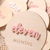 A set of light pink wooden baby milestone cards with the word eleven months engraved on them.