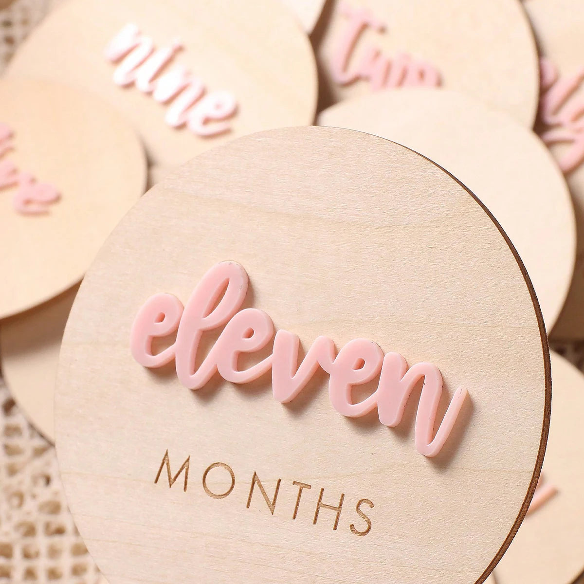 A set of light pink wooden baby milestone cards with the word eleven months engraved on them.