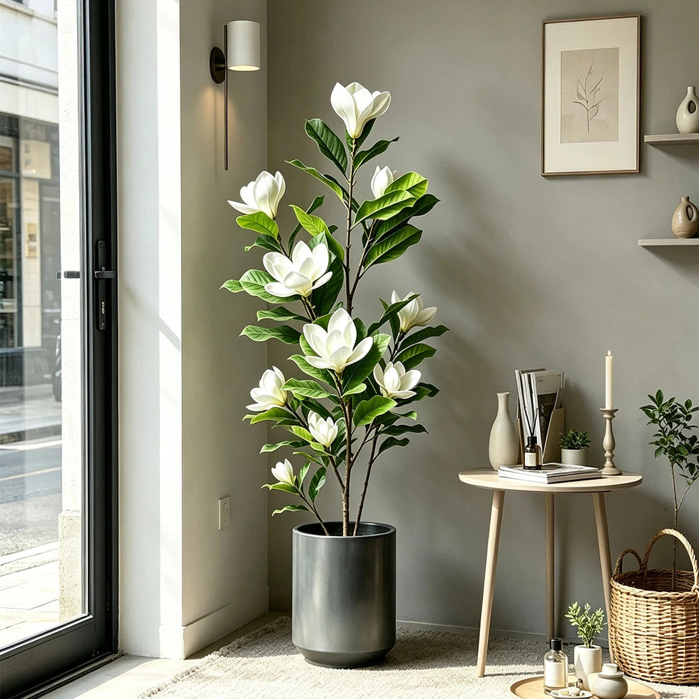 A tall artificial magnolia tree with white silk flowers in a dark pot displayed indoors.